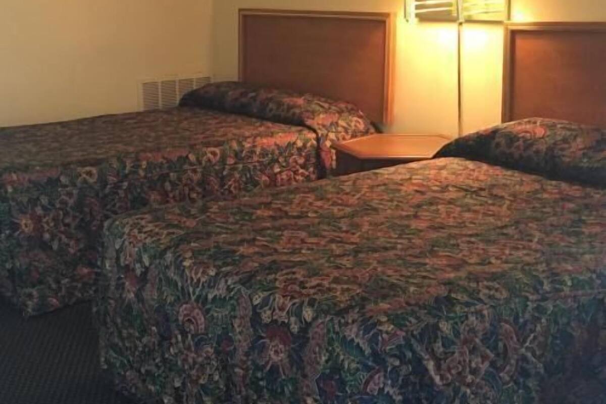A hotel room with two beds, a nightstand, a lamp, and a painting on the wall.