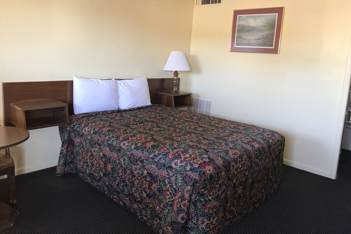 A hotel room with a bed, a nightstand, a lamp, a picture on the wall, and a small table.