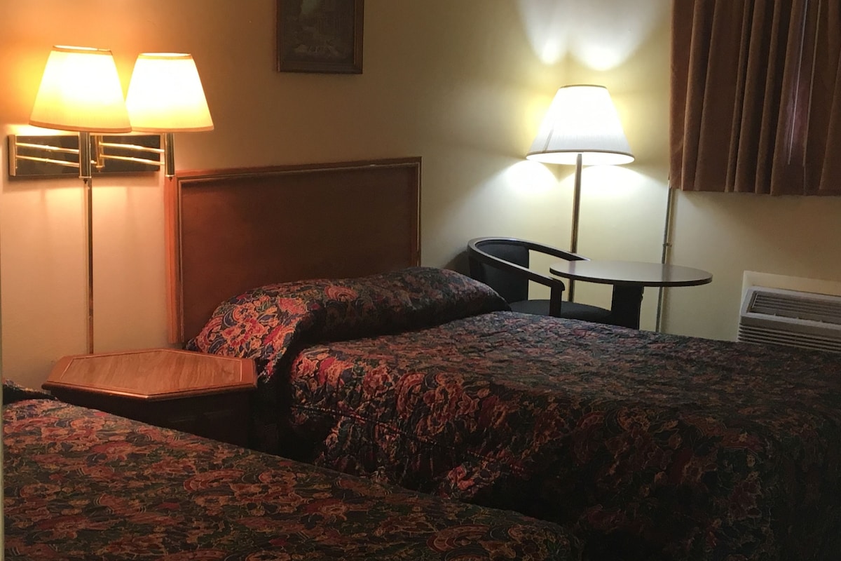 A hotel room with two beds, a desk, and two lamps.