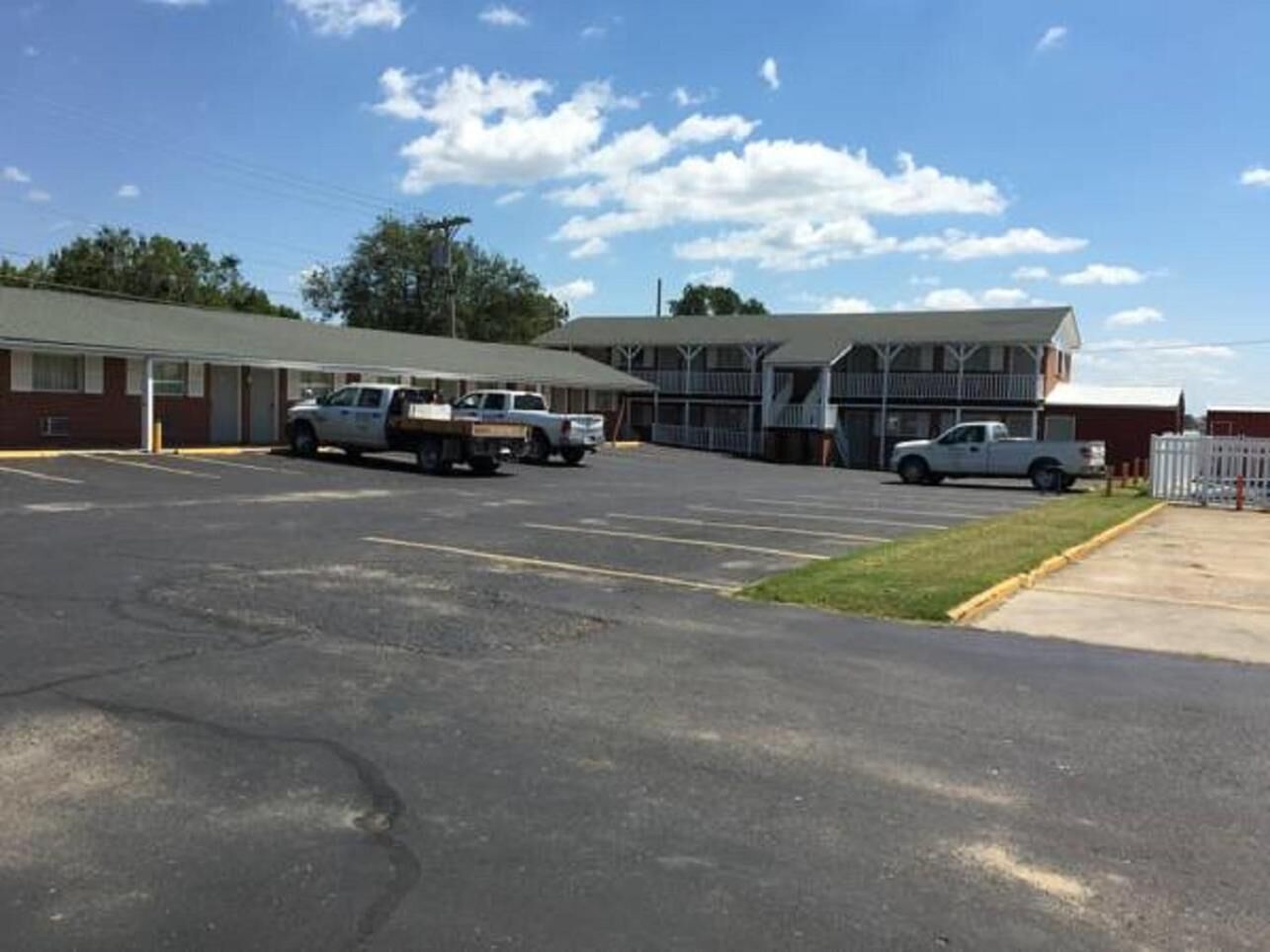 A parking lot with several vehicles, a building with a porch, and a fenced area.