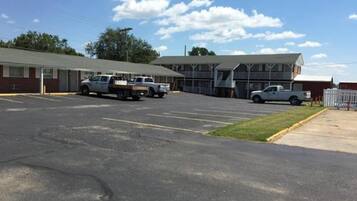 A parking lot with several vehicles, a building with a porch, and a fenced area.
