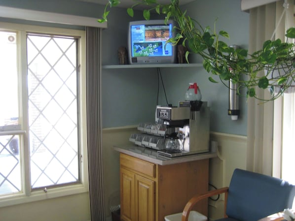 Una habitación con televisión en un estante, ventana con vistas, un armario y una silla.