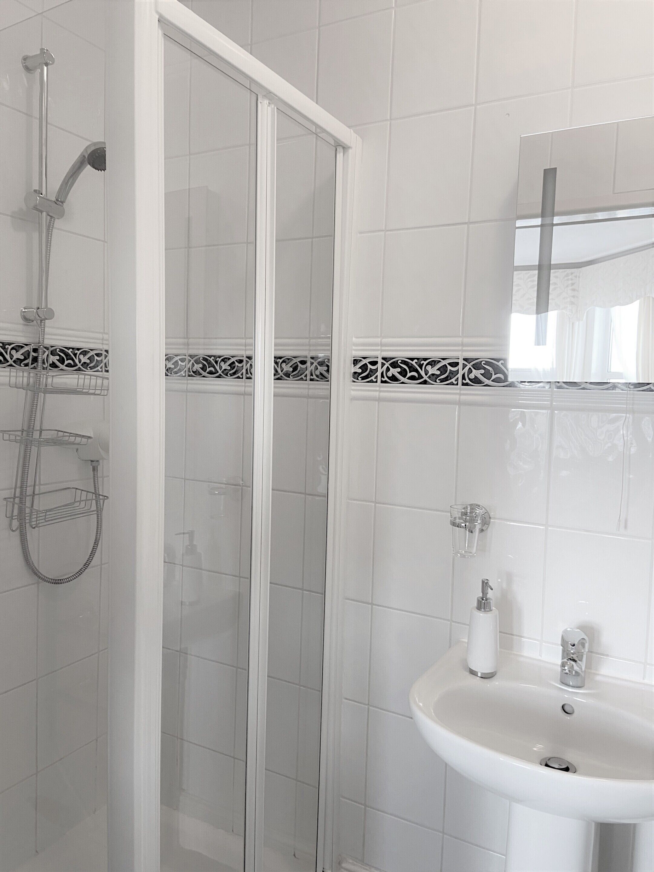 A bathroom with a glass shower enclosure, a white sink with a mirror above it, and decorative tiles on the walls.