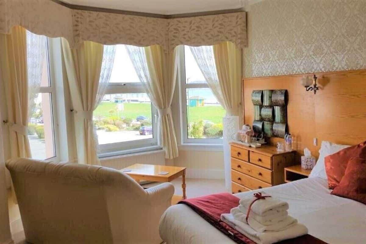 A hotel room with a bed, a chair, a nightstand, and a view of the outdoors.
