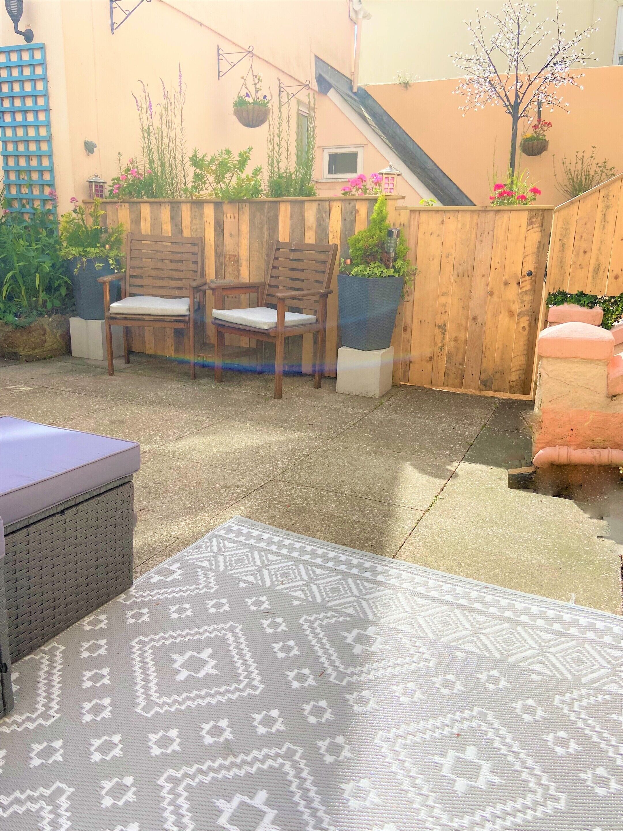 A patio area with two wooden chairs, a cushioned bench, and a patterned rug.
