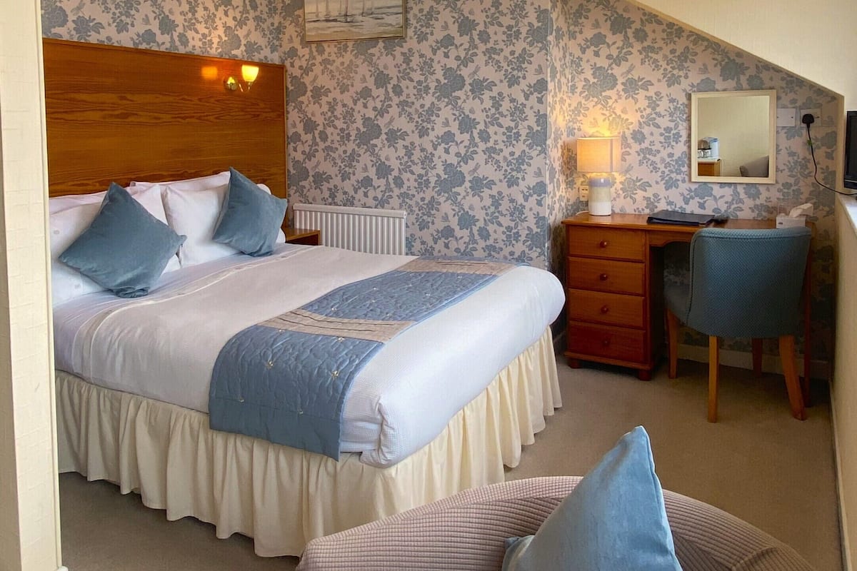 A bedroom with a bed, a desk, a chair, and a mirror.