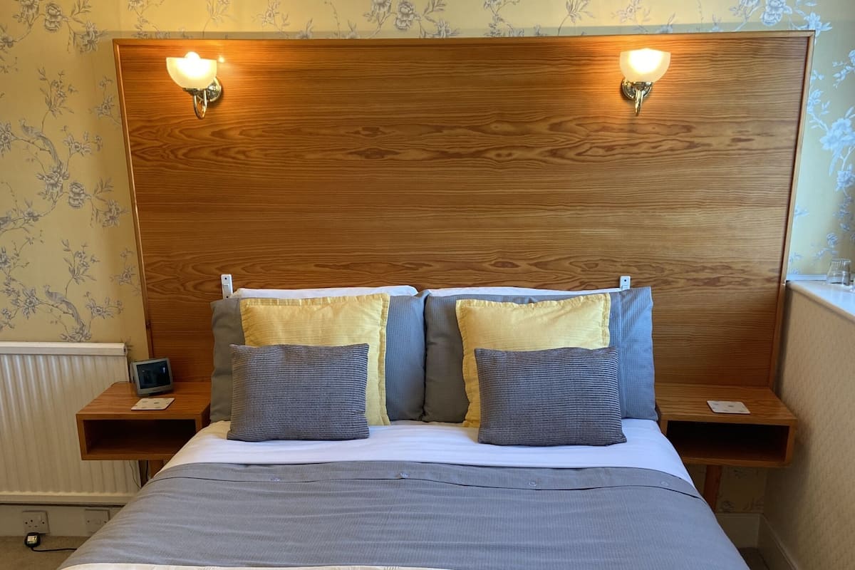 A neatly made bed with a wooden headboard, two bedside tables with lamps, and floral wallpaper.