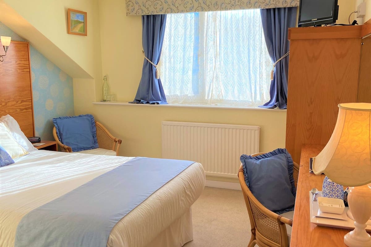 A hotel room with a bed, a desk with a lamp, a chair, a television, and a window with curtains.