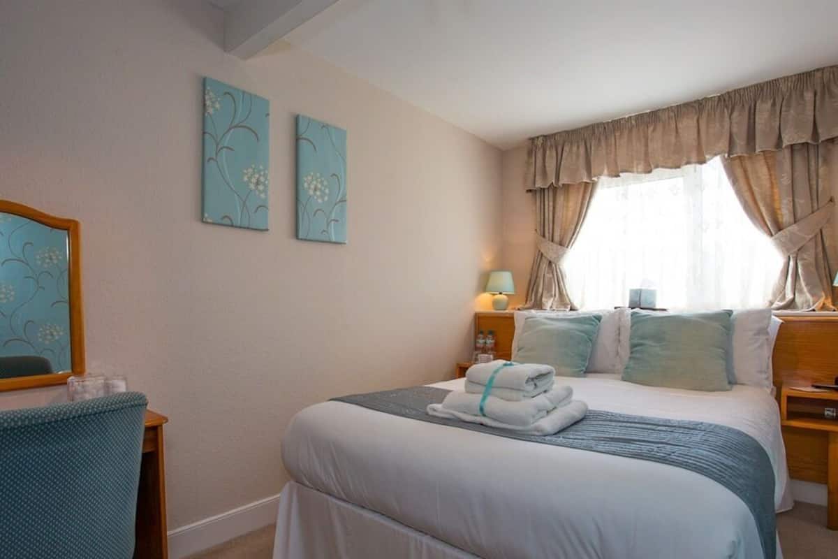 A neatly made bed with a blue and white duvet, a bedside lamp, and a window with curtains.