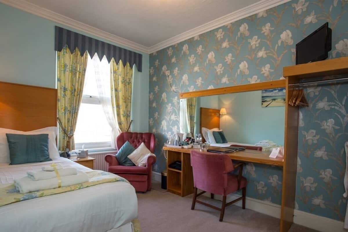 A bedroom with a bed, a desk, a chair, and a television.