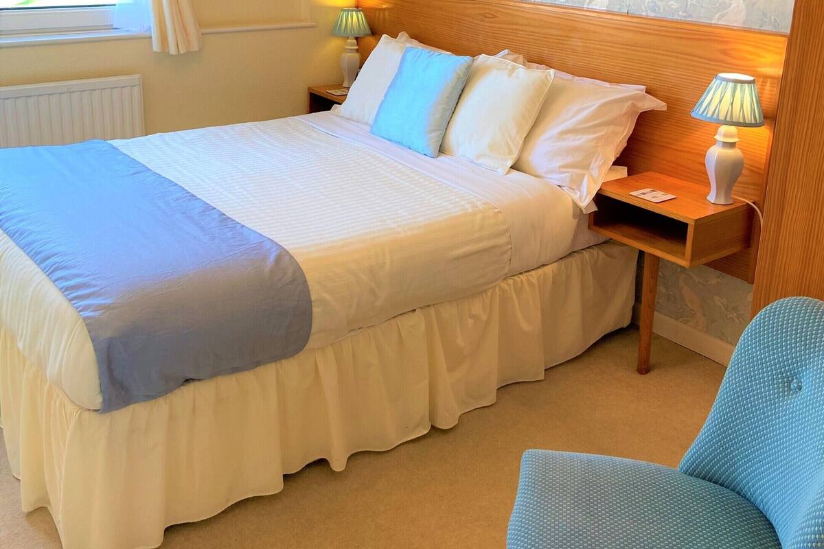 A bedroom with a large bed, a nightstand, a chair, and a window with curtains.