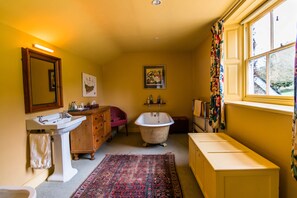 A bathroom with a wooden cabinet, a white sink, a bathtub, and a window with curtains. - Church House Kington (Kington)