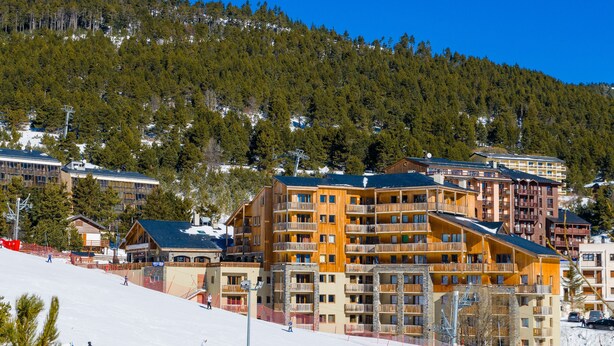A ski resort with multi-story buildings, ski slopes, and a forested mountain backdrop.