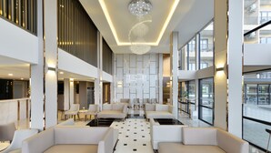 A spacious lobby with modern seating, a central chandelier, and large windows offering views of the outside. - BS RESIDENCE Suvarnabhumi (Bangkok)