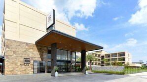 A hotel entrance with a covered walkway, large windows, and a stone facade. - BS RESIDENCE Suvarnabhumi (Bangkok)