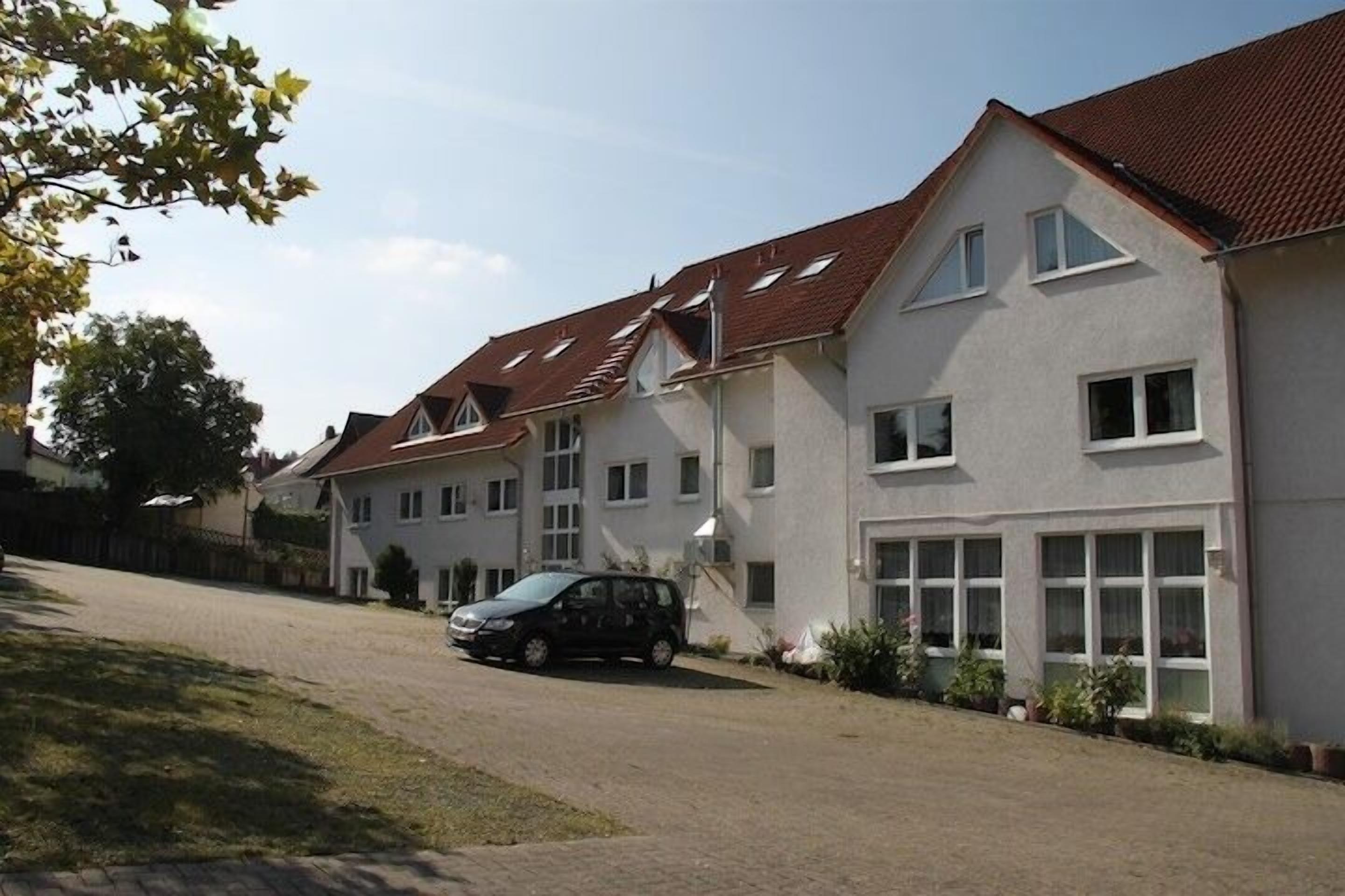 A two-story residential building with a sloped roof, multiple windows, and a car parked in the driveway.