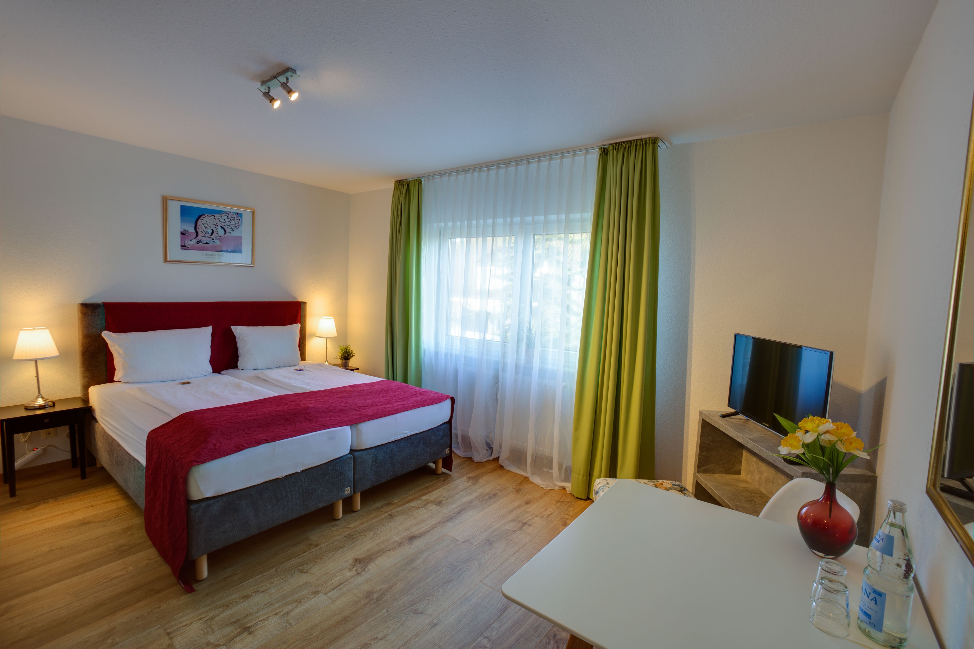 Una habitación de hotel con cama doble, escritorio, televisor y ventana con cortinas.