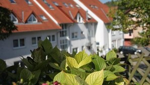 Filas de casas con techos rojos y paredes blancas, vistas desde un jardín con follaje verde en primer plano.