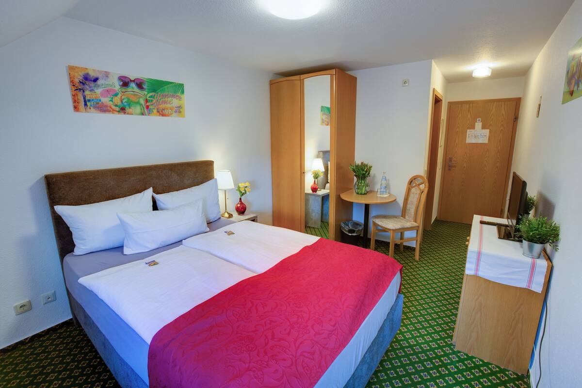 A hotel room with a bed, a desk, a chair, a mirror, and a door.