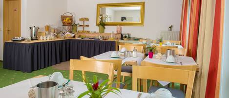 Un espace repas avec des tables préparées pour le petit-déjeuner, comprenant un buffet proposant divers aliments et un miroir placé au-dessus des tables.