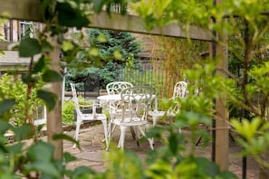 A patio with white metal chairs and tables, surrounded by greenery and a wooden fence. - My Edinburgh Life (Edinburgh)