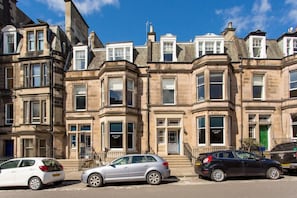 A row of traditional terraced houses with bay windows, a green door, and a visible shop sign. - My Edinburgh Life (Edinburgh)