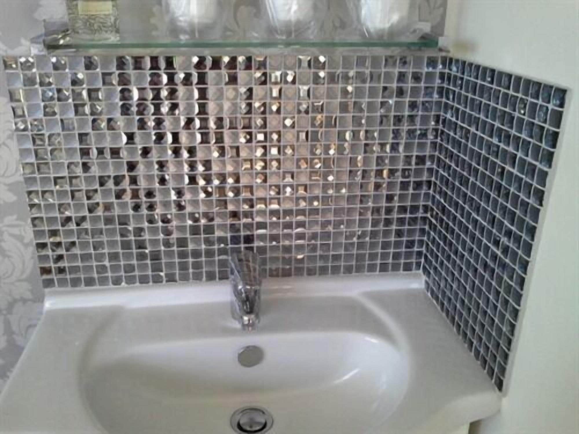 Un baño con lavamanos, un estante de vidrio sobre el lavamanos y una pared con azulejos formando un patrón de diamantes.