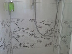 A bathroom with a shower, a green bottle, and floral-patterned tiles. - Ellerbrook House (Windermere)