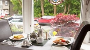 A dining table set with plates, a teapot, and a pitcher, with a view of trees and parked cars outside. - Ellerbrook House (Windermere)