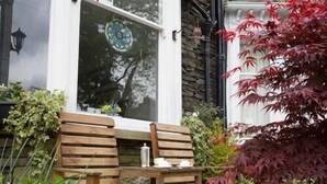 A wooden bench with cushions, a stone wall, and a window with a decorative glass panel. - Ellerbrook House (Windermere)