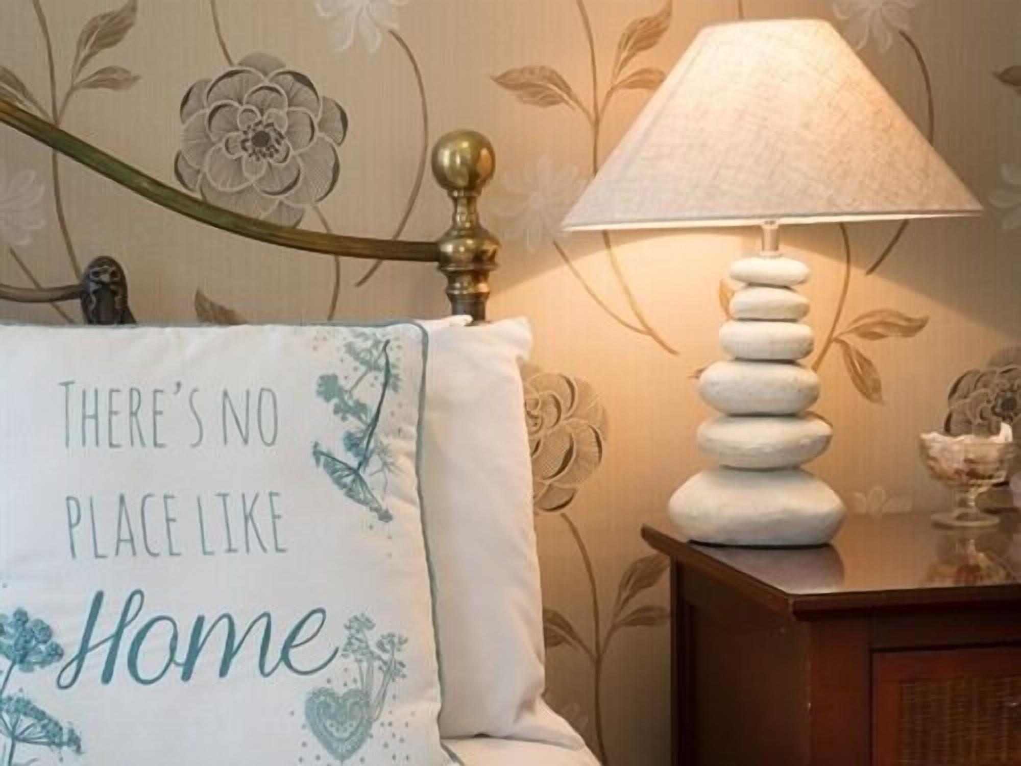 A bedroom with a bed, a bedside lamp, and a wall with floral wallpaper.