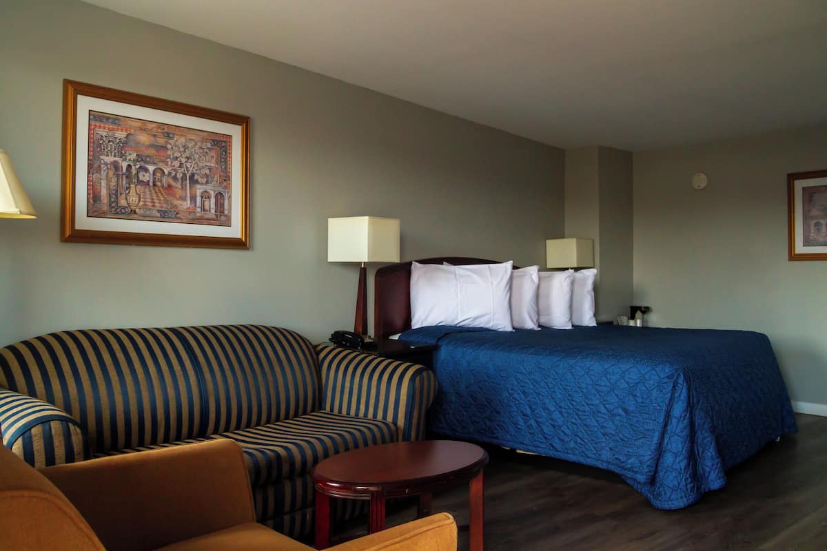 A hotel room with a bed, a sofa, a small table, and a lamp.
