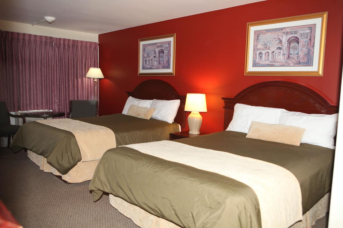 A hotel room with two beds, a desk, a chair, and a lamp.