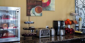 Un comptoir de cuisine avec un grille-pain, une machine à café et une vitrine contenant des pâtisseries.