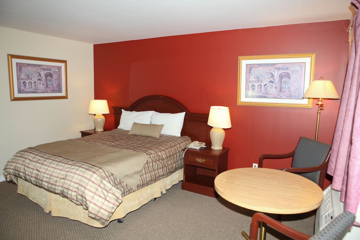 A hotel room with a large bed, two bedside tables with lamps, a small round table, and two chairs.