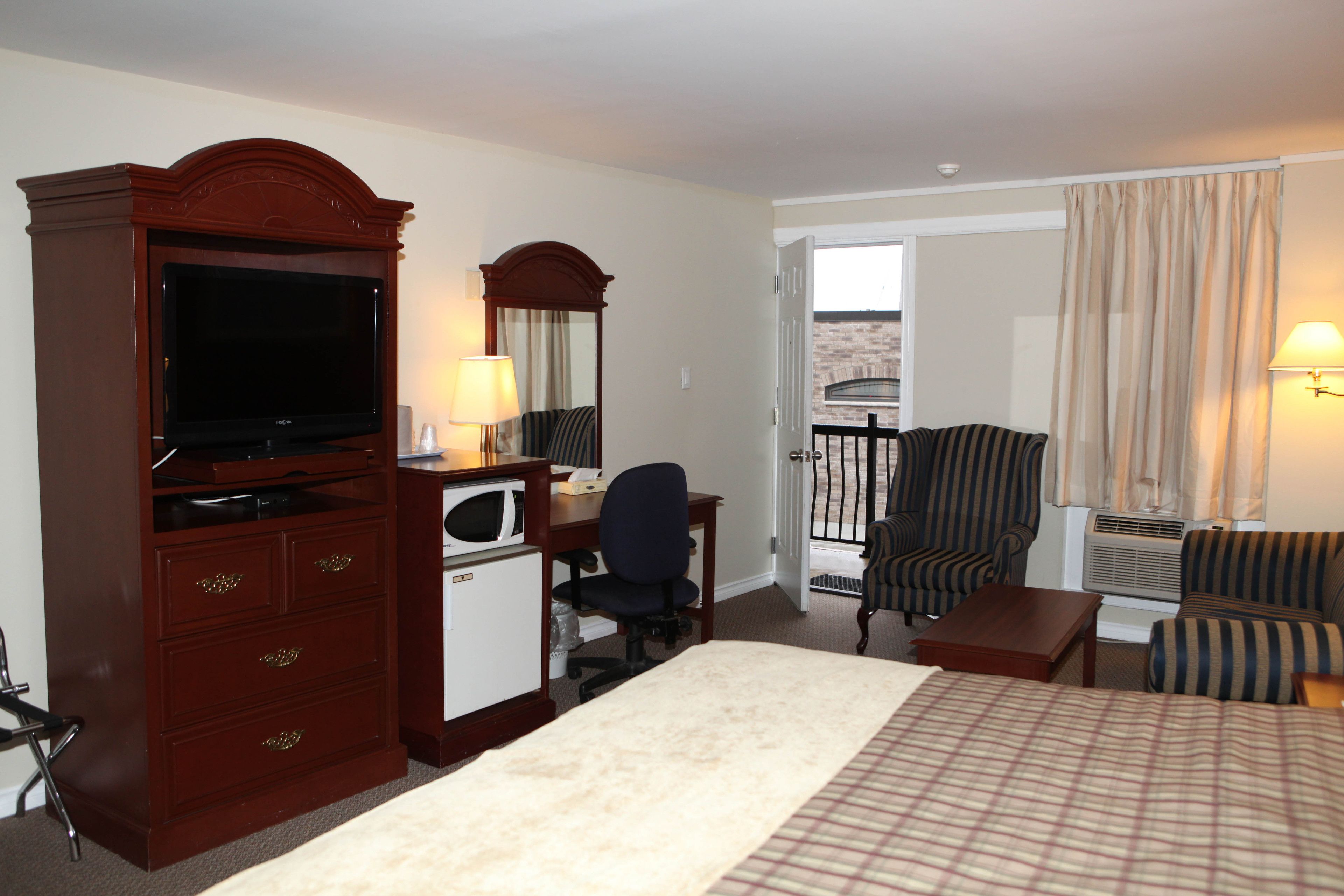 A hotel room with a large bed, a desk with a computer, a television, a chair, and a balcony with curtains.