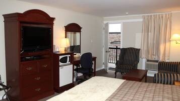 A hotel room with a large bed, a desk with a computer, a television, a chair, and a balcony with curtains.