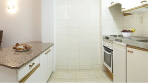 A kitchen with white cabinets, a granite countertop, a stove, and a bowl of fruit. - Catalonia Gardens (Salou)