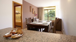 A dining area with a table set for four, a plate of pastries, and a view of a balcony. - Catalonia Gardens (Salou)