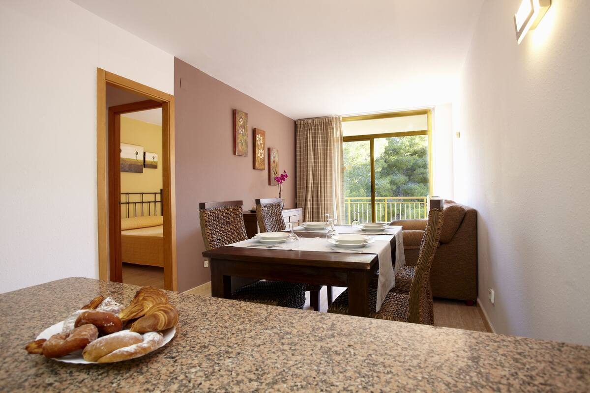 A dining area with a table set for four, a plate of pastries, and a view of a balcony.