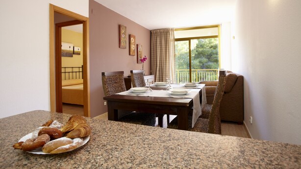 Un coin repas avec une table dressée pour quatre personnes, une assiette de pâtisseries et une vue sur un balcon.