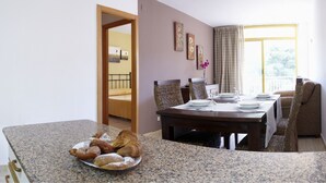 A dining area with a granite countertop, a dining table set with plates and cutlery, and a plate of pastries. There are wicker chairs and a sofa in the background. - Catalonia Gardens (Salou)