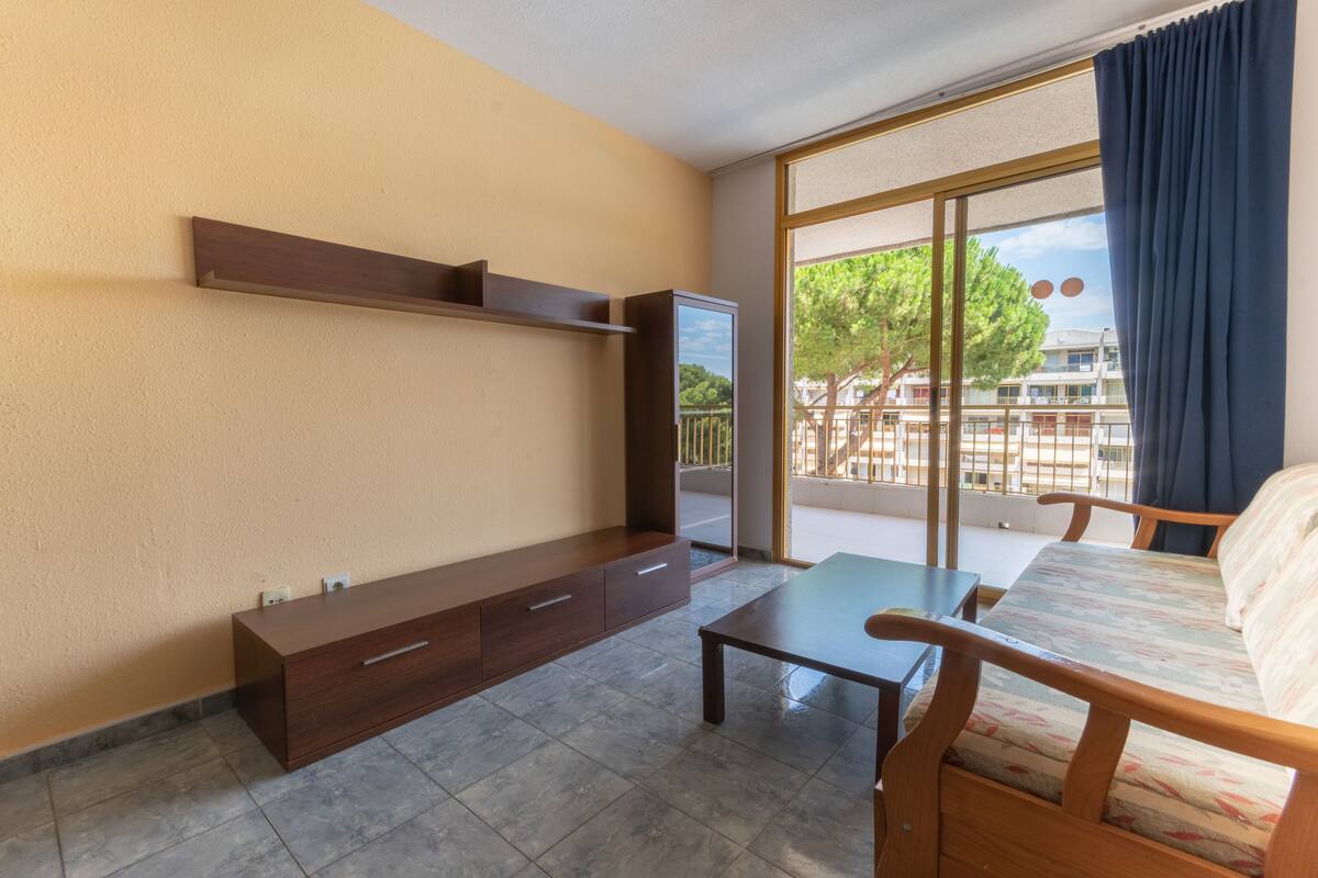 A room with a sofa, a small table, a cabinet, and a large window with a view of buildings and trees.