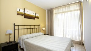 A hotel room with a single bed, a nightstand with a lamp, and a window with sheer curtains. - Catalonia Gardens (Salou)