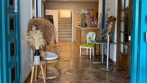 A hallway with a tiled floor, a wicker chair, a small table with a vase, and a dining area with chairs and a table. - Hôtel Restaurant Le Filosorma (Galeria)