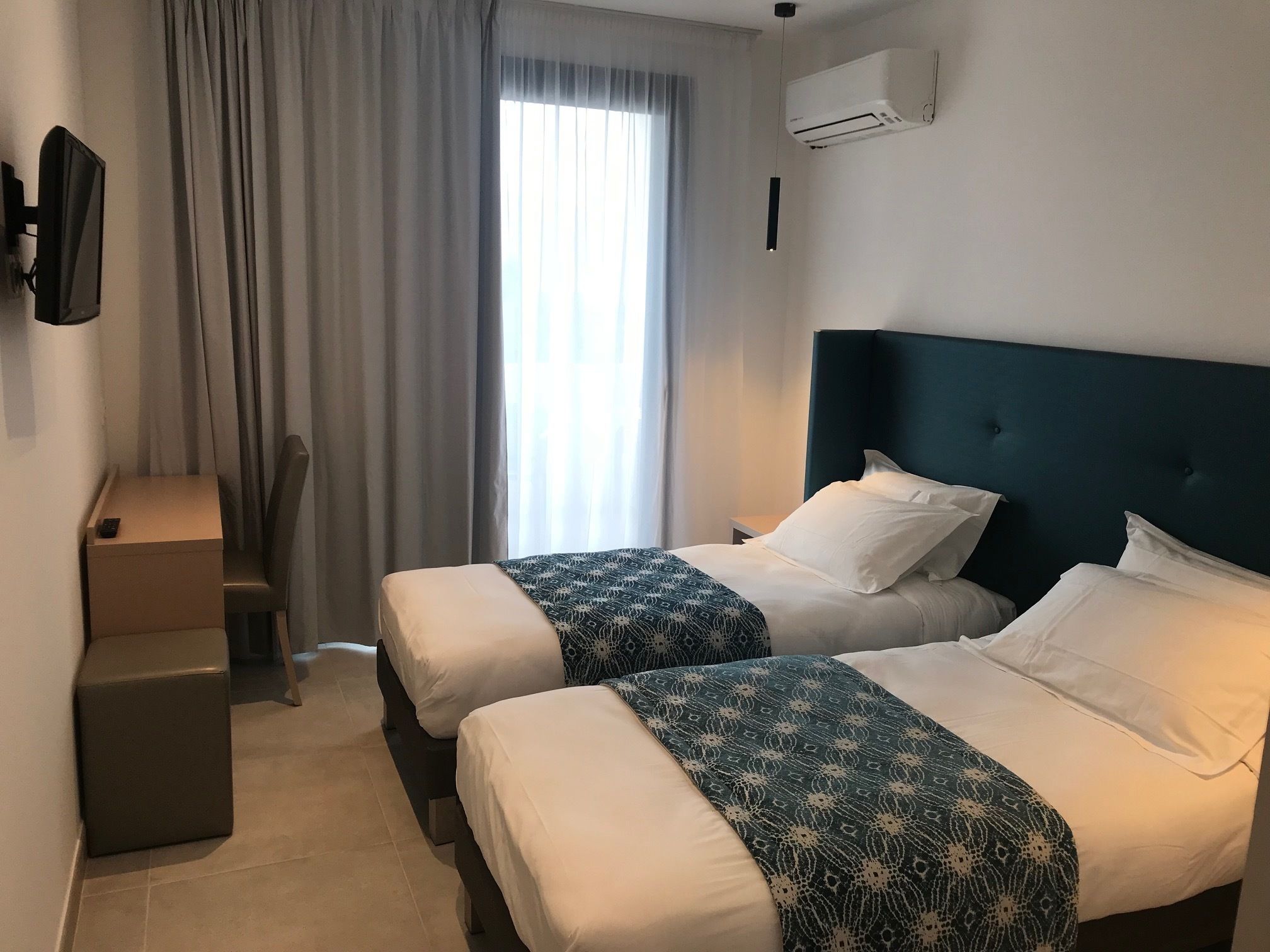 Une chambre d’hôtel avec deux lits, un bureau, une chaise, une télévision et un appareil de climatisation.