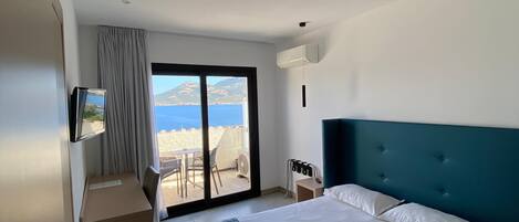 Ett hotellrum med en säng, ett skrivbord, en stol, en tv och utsikt över havet.