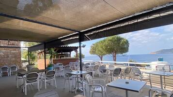 An outdoor seating area with tables and chairs, a stone wall, and a view of the sea.