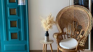 A teal door with decorative panels, a wicker chair with a cushion, and a small table with a vase of dried plants. - Hôtel Restaurant Le Filosorma (Galeria)