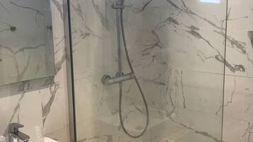 Une salle de bain moderne avec une douche à parois de verre, un mur recouvert de carreaux de marbre, un lavabo blanc et un miroir.
